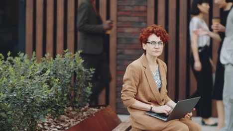 Redhead-Businesswoman-Working-on-Laptop-on-Street